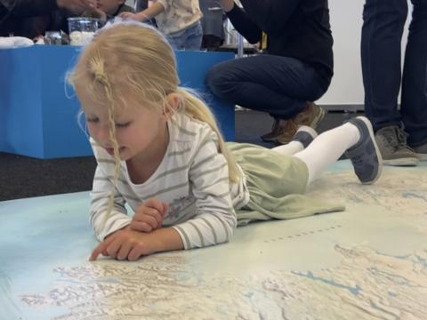 Ung stúlka liggur á stóru korti af Íslandi og rýnir í landið